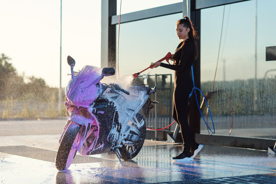 Attractive girl washes a motorcycle at self service car wash with high pressure water.