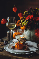 Beautiful elegant table setting for candlelight Thanksgiving Day dinner or Halloween party at home. Fancy dishware, porcelain plates. Floral centrepiece, pumpkins and burning candles as decor