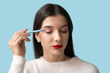 Beautiful young woman with brush applying eyeshadows on blue background