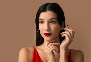 Fototapeta premium Beautiful young woman with red lipstick on brown background