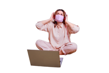 A woman in a medical mask listens to music and rests on a home bed, isolated on a white background. Cute woman in a pink mask on her face sits in headphones on a yellow bedspread.