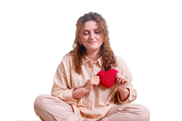 A woman confesses her love via the Internet, isolated on a white background. Happy woman sits with a cat on a bed in a bedroom with a heart in her hands