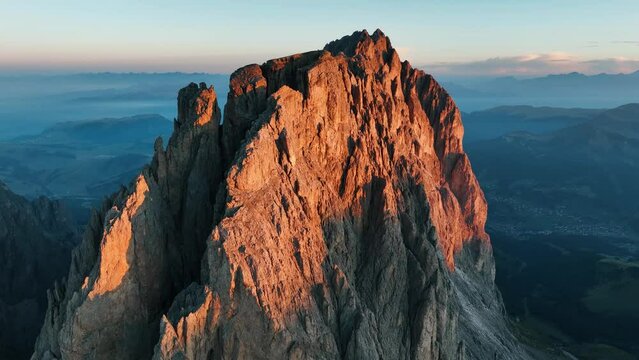 Sorvolo lento della cresta di una vetta dolomitica su uno sfondo di cime e foschia al tramonto