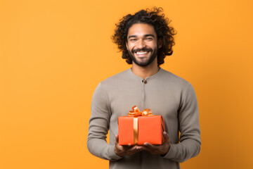 Happy smiling man holding gift box Medium shot portrait photography of a grinning mature man holding a gift against a tangerine orange background. - obrazy, fototapety, plakaty