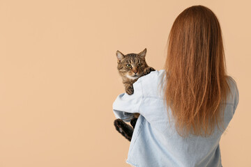 Woman with cute tabby cat on beige background, back view