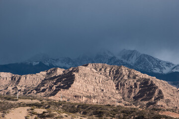 Fototapeta premium red mountain lit by the sun with gloomy snow-capped mountains on the background