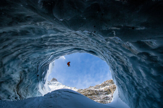 Person skiing on snowy mountain seen through cave