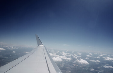 Fototapeta na wymiar Wing of modern aircraft flying in cloudy blue sky during trip