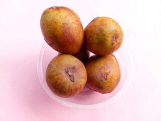 pile of ripe sapodilla fruit in a bowl on a pink background. fresh and healthy fruit.