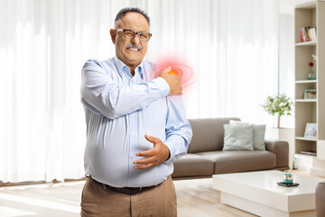Mature man standing at home and holding shoulder with red spot
