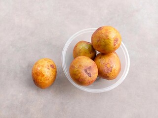 pile of ripe sapodilla fruit in a bowl on a gray background. fresh and healthy fruit.