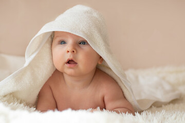 Cute little infant wrapped in white towel after bath or shower in bedroom. Close-up portrait of baby boy. Baby care concept. Selective focus