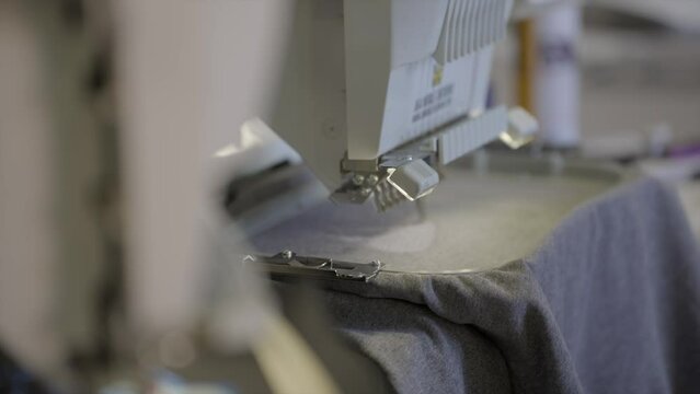 This video shows a close up, sideview of an automatic embroidering machine as it stitches on black fabric. 