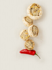 Top quality stuffed mushrooms cups and red chilly pepper on a cooking paper. High quality product with breadcrumbs, cheese and herbs for baking in oven.