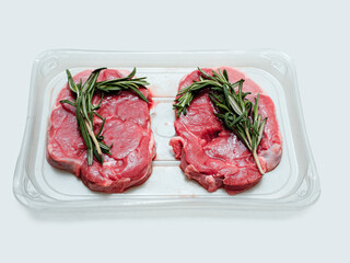 Two boneless lamb leg steaks on a plastic tray and rosemary green spicy herb. Uncooked high quality meat product with rich taste and vivid color.