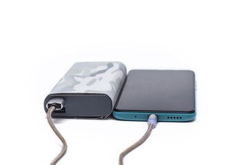 Modern smartphone is charged using a portable charger via a cable. Power bank in a camouflage case isolated on a white background. External battery for gadgets.