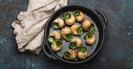Escargots de Bourgogne Cooked Snails with Garlic Butter and Parsley in black cast iron pan on rustic stone background top view, traditional French Delicacy .