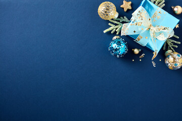 Xmas greeting card template. Luxury blue Christmas background with glittering gift box, golden balls, decorations, fir branches in corner of greeting card.