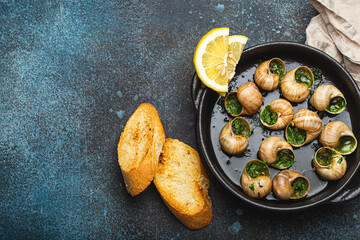 Escargots de Bourgogne Snails with Garlic Butter and Parsley in black cast iron pan with Lemon and Toasted Baguette Slices on rustic stone background top view, traditional French Delicacy, copy space. - obrazy, fototapety, plakaty