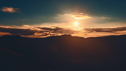 Sunrise cloudscape sky over mountain range silhouette. Dramatic clouds flow in dark sky, sun glow rise over mountain peak with golden light beams. Beautiful morning nature landscape.