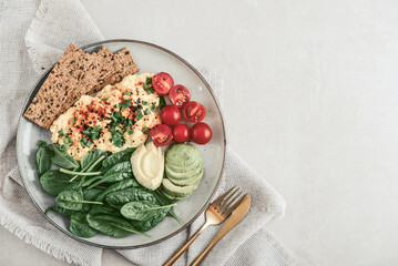 Scramble eggs with cherry tomatoes, fresh spinach leaves, avocado and crispbreads