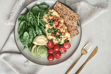 Scramble eggs with cherry tomatoes, fresh spinach leaves, avocado and crispbreads