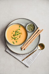 Pumpkin soup in a bowl with pumpkin seeds, green onions and breadsticks