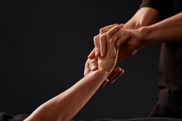 a male masseur doing a hand massage to a girl on a dark background,
