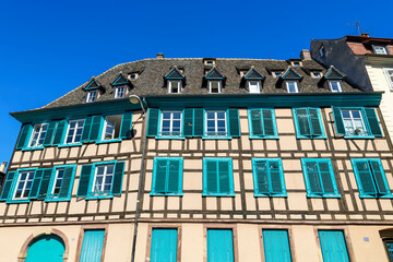 A large half timber frame building with turquoise shutters in the medieval old town center of Strasbourg, France. - Powered by Adobe