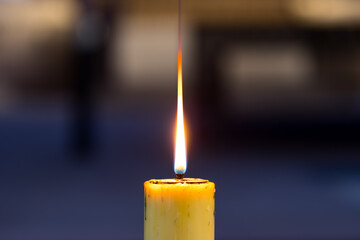 A burning candle in a church with a blurred background. The flame is visible.