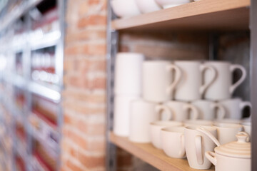 Variety of earthenware is neatly arranged on shelves of rack in pottery shop
