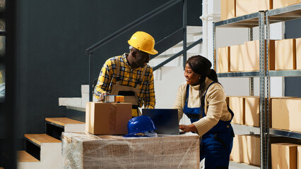 Happy group of employees laughing and checking boxes, preparing products in packages for shipment and distribution. Young people having fun at work in warehouse, stock supplies. Tripod shot.