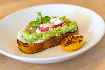 Avocado toast with cheese, pickled onions with parsley and lemon on a white plate