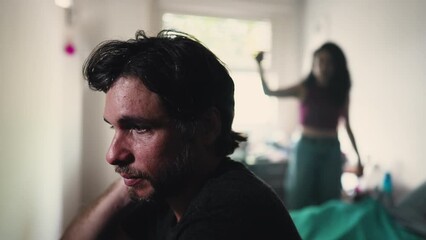 Stressed boyfriend listening to screaming girlfriend arguing with him in background. couple fighting in bedroom. Male person sitting by bedside suffering from a bad relationship - Powered by Adobe
