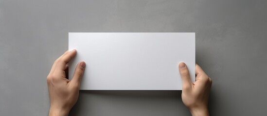 Hands holding a blank white business card on a gray background.
