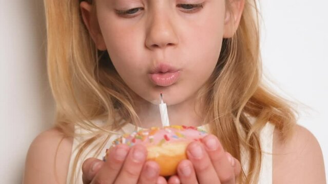 A girl child blowing out a candle on a pink donut. Happy Birthday or anniversary concept. Make a wish slow motion full HD birthday video.