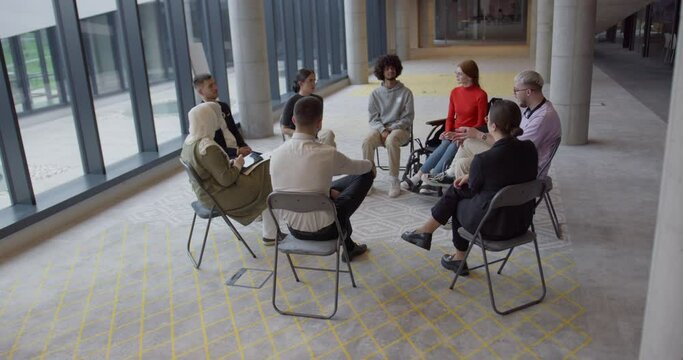 A diverse group of young business entrepreneurs gathered in a circle for a meeting, discussing corporate challenges and innovative solutions within the modern confines of a large corporation