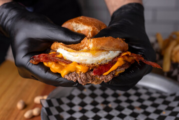 hands in black gloves holding beef burgers with onion chedar cheese and potato bun