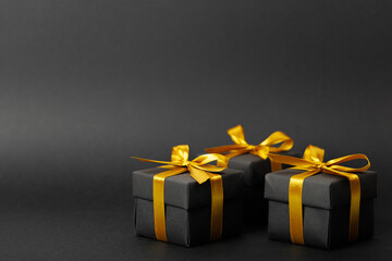 Black gift box with golden ribbon bow on black background