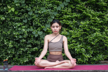Young Asian woman doing yoga, meditation on a calm yoga mat in a green park in the early morning. Young woman wearing brown yoga clothes Yoga concept