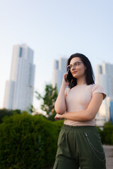 Fototapeta premium Beautiful girl with dark hair and talking on a phone. Three skyscrapers in the background.