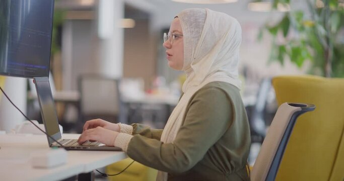 A businesswoman in a hijab is seen working on a computer in a modern office, highlighting inclusivity and professionalism in a diverse workplace