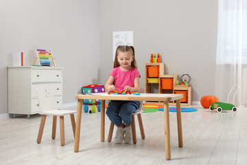 Motor skills development. Girl playing with colorful wooden arcs at white table in kindergarten