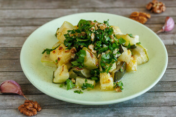 Healthy homemade salad of young grilled zucchini, garlic and nuts, seasoned with vegetable oil in a plate on wooden table background. Vegetarian food