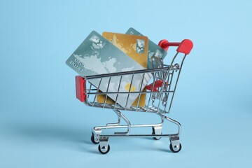 Small metal shopping cart with credit cards on light blue background