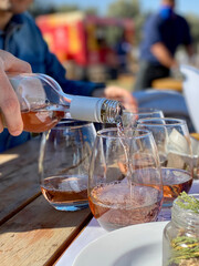 Rosé wine being poured into a glass. The bottle is held by a person's hand and the glass is one of...