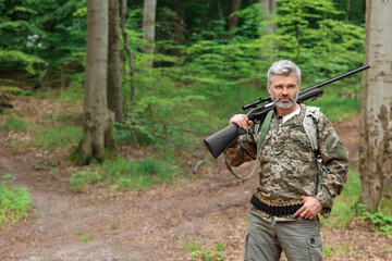 Fototapeta premium Man with hunting rifle wearing camouflage in forest. Space for text