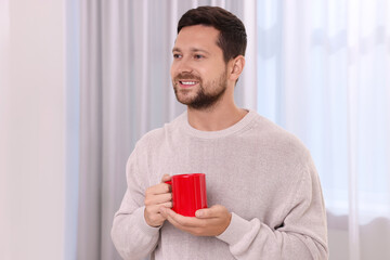Happy man holding red ceramic mug at home