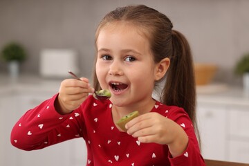 Cute girl eating tasty fresh kiwi indoors