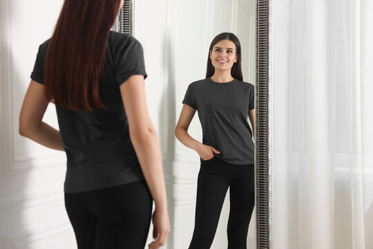 Beautiful young woman in stylish black jeans near mirror indoors